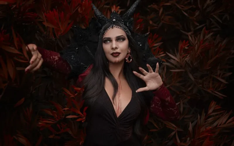 Mysterious vampire woman posing in the forest with a dark costume.