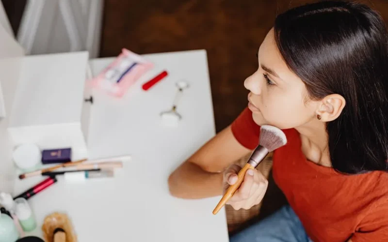 Top view of a woman applying makeup with a brush at a vanity table.