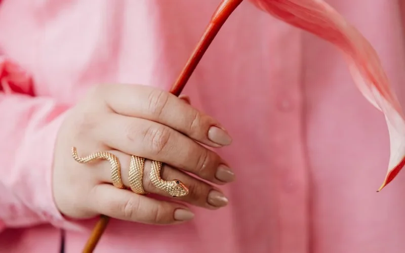 Close-up of a hand with manicured nails holding a flower and wearing a gold snake ring.