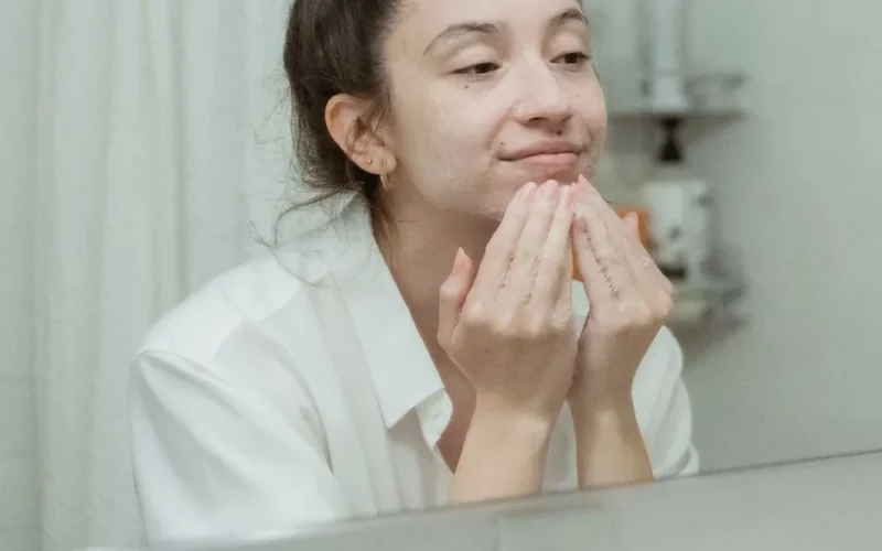 A woman applies facial cream, enjoying her skincare routine in front of a bathroom mirror.