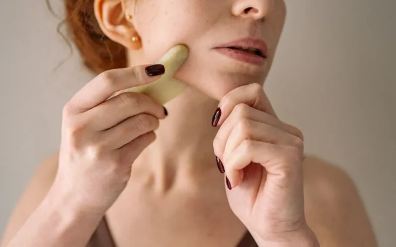 Close-up of a woman using a gua sha stone on her face, emphasizing self-care and beauty routine.