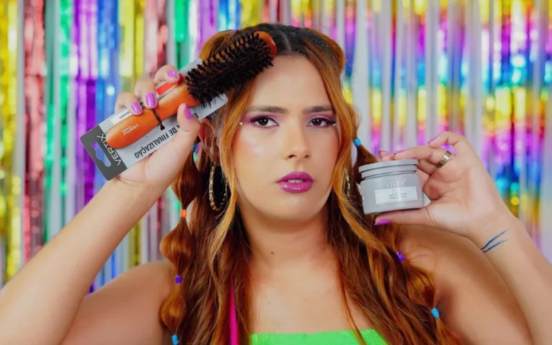 A woman holding a hairbrush and styling cream in a vibrant, colorful setting.
