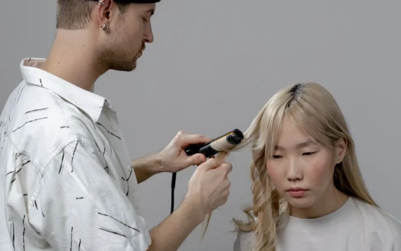A hairstylist using a curling iron to style a woman's hair in a salon setting.