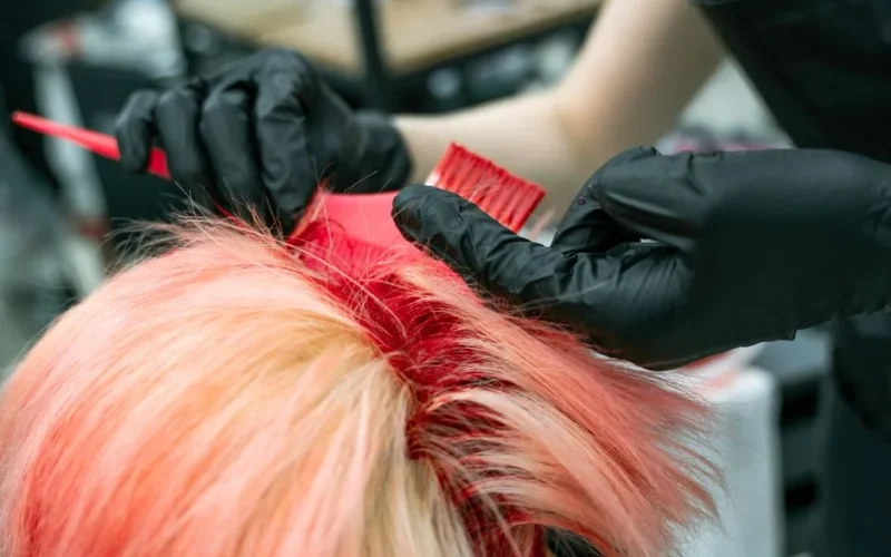 Close-up of vibrant hair coloring process with gloved hands applying dye.
