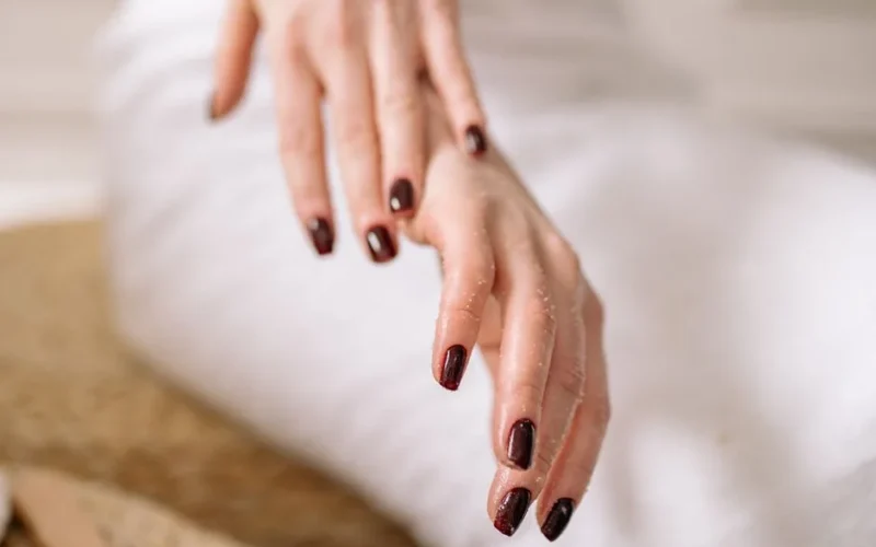 Close-up of a woman's hand with dark polished nails against a spa backdrop.