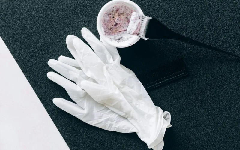 Flat lay of hairdressing tools including dye brush, latex gloves, hair dye bowl, and comb.