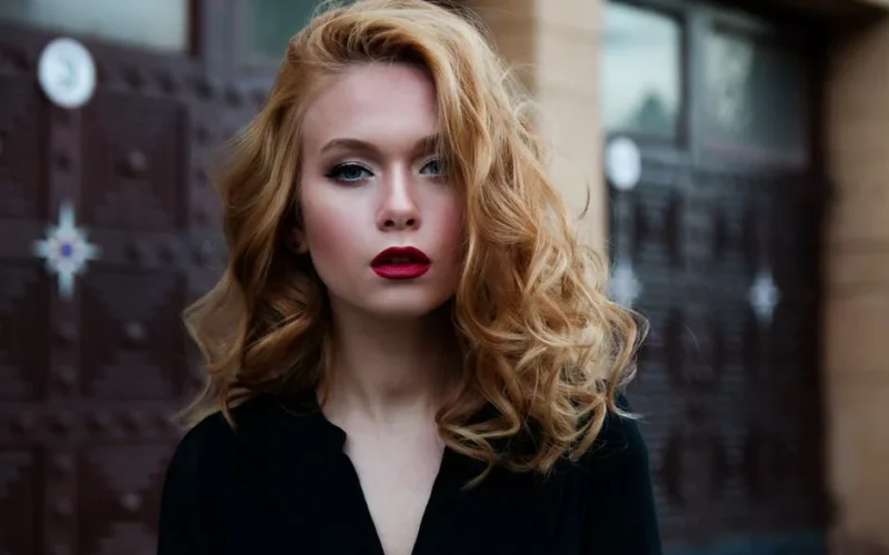 Elegant portrait of a woman in a black top with striking red lips and flowing blond hair.