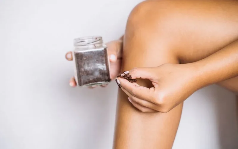 Close-up of a person's leg applying coffee scrub for skin exfoliation and body care.