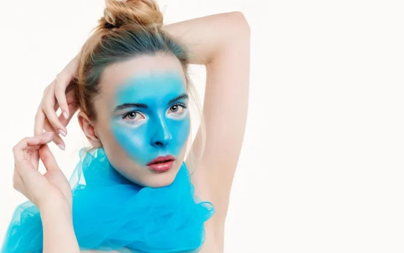 Elegant portrait of a woman with blue face paint and scarf against a light background.