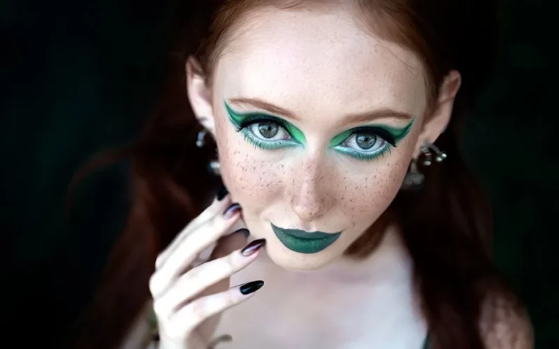 Close-up of a woman with striking green makeup, red hair, and freckles. Captivating and artistic portrait.