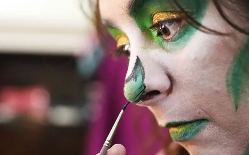 Detailed shot of a person applying green face paint meticulously with a brush.