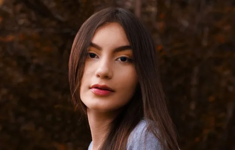 Close-up portrait of a young woman with long hair in a natural autumn setting.