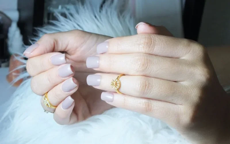 Close-up of beautiful manicured hands showcasing grey nails and gold rings in a serene setting.