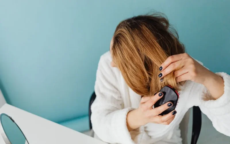 A woman in a bathrobe combs her hair reflecting self-care and relaxation.