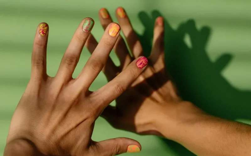 Vibrant nail art on hands casting shadows on a bright green background.