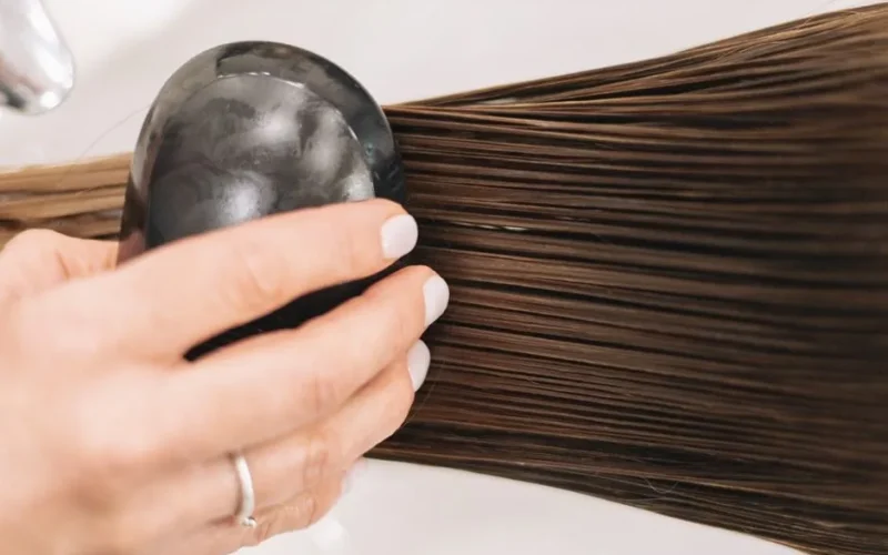 Close-up of a woman brushing long brown hair with a black brush, highlighting hair care and grooming.