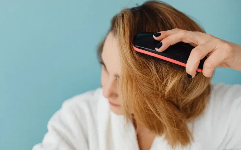 Close-up of a woman with brown hair brushing her hair in a bathrobe, representing a daily grooming routine.