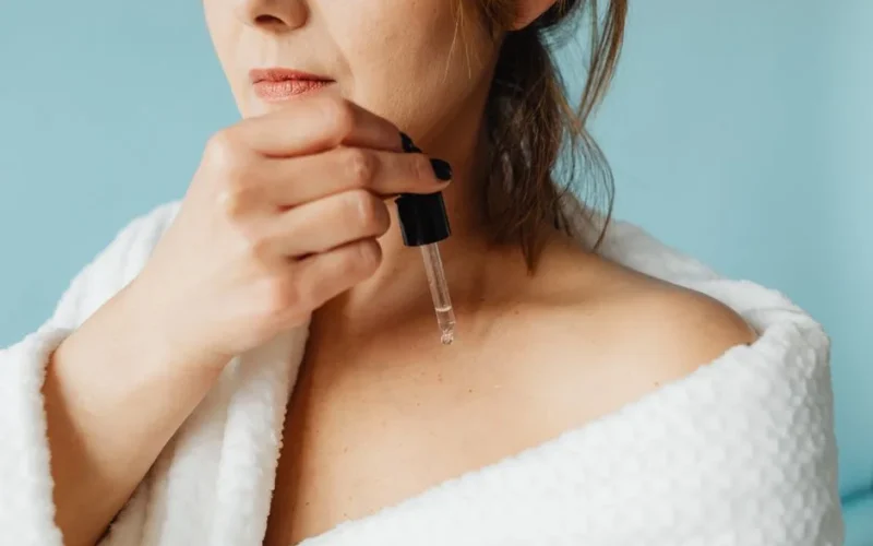 Close-up of a woman in a bathrobe applying serum for skincare routine.