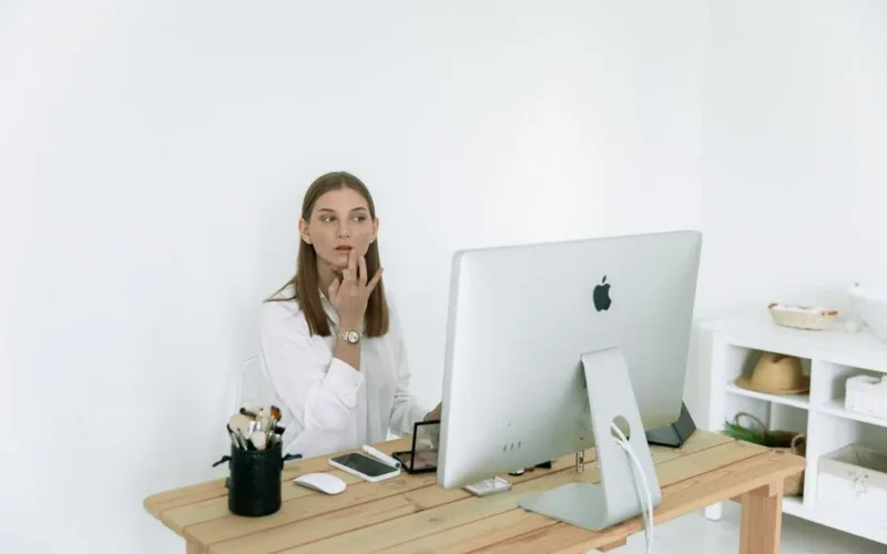 Woman applying makeup at her desk in a modern home office setting.