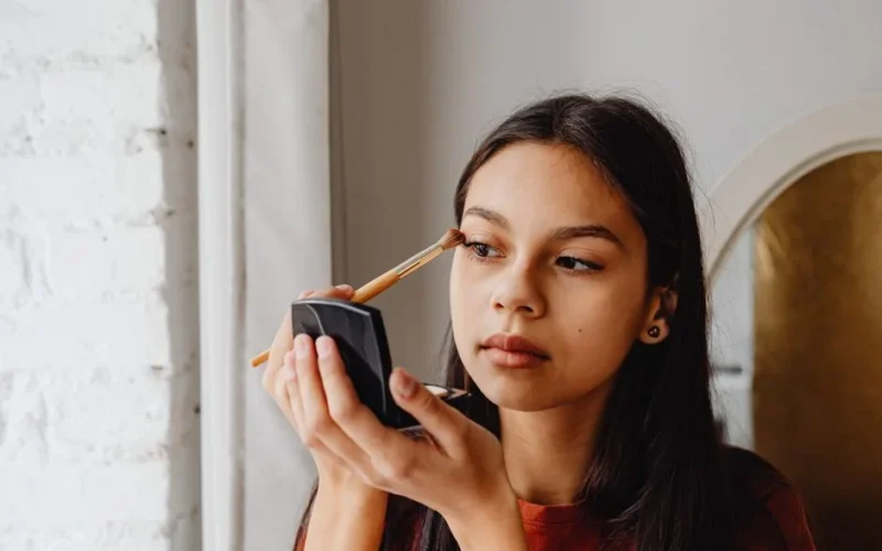 A focused young woman applying eyeshadow with a makeup brush indoors.