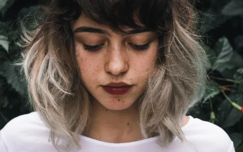 Close-up portrait of a young woman with freckles and two-toned hair outdoors.