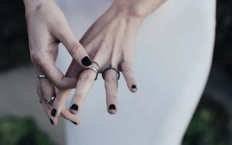 Elegant close-up of hands showcasing multiple rings and black nail polish in a minimalistic background.