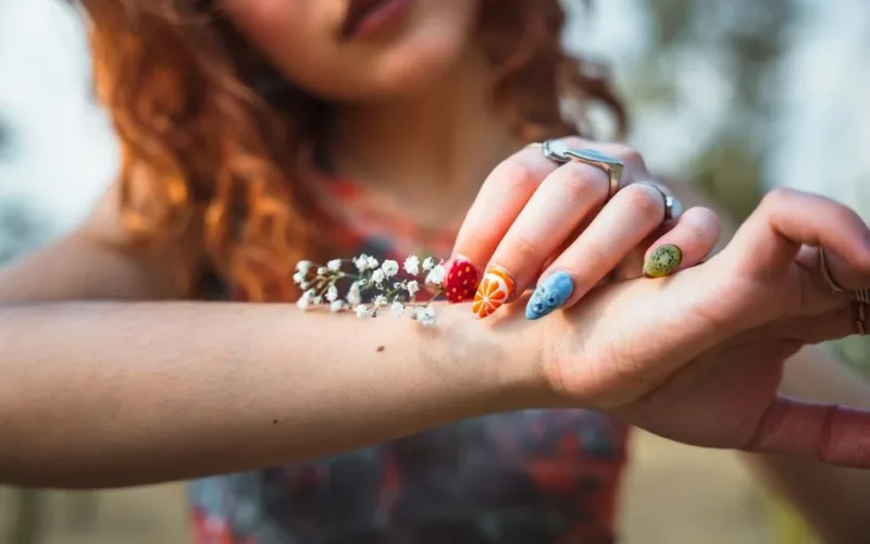 Close-up of a woman's hand showcasing vibrant and artistic nail art designs outdoors.