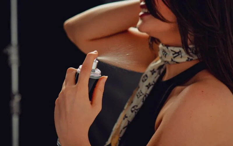 Woman with long hair spraying perfume on her neck, close-up view for a fresh and stylish image.