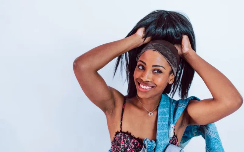 Portrait of a smiling woman adjusting her wig while wearing a denim jacket, indoors.