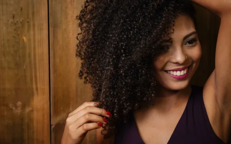 Close-up portrait of a smiling woman with curly hair touching her locks indoors.