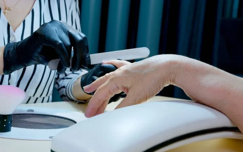 Close-up of a manicurist filing nails, providing professional salon service with gloves.