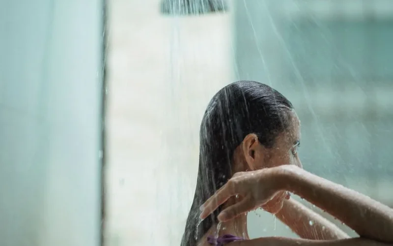 Side view of lady with closed eyes standing in shower and enjoying water