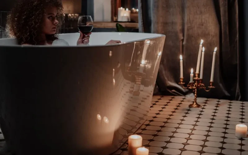 Woman relaxing in a candlelit bath enjoying a glass of wine.