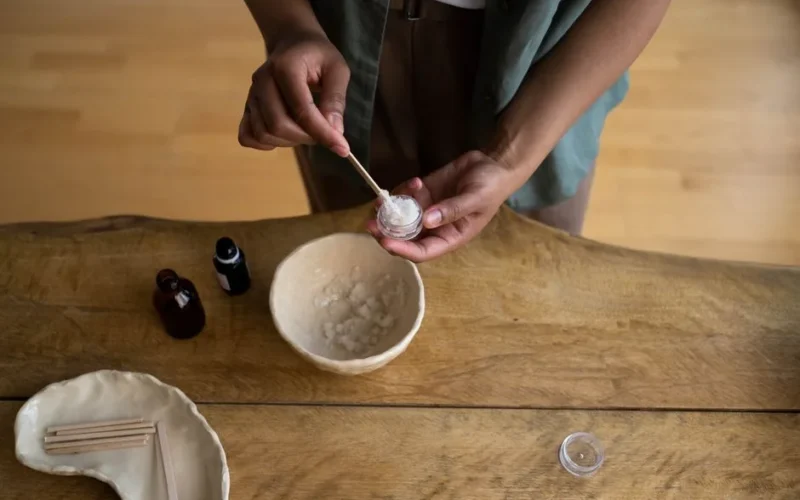 Hands transferring homemade skincare into a container on a wooden table.