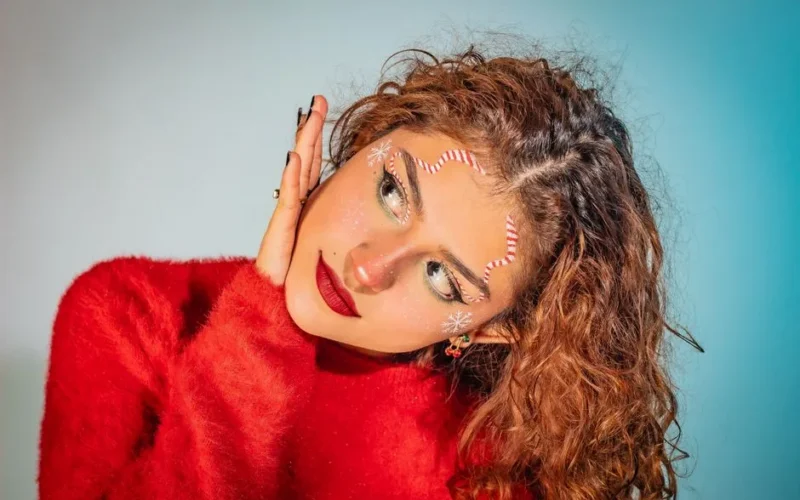 A close-up portrait of a woman in festive makeup and red sweater, exuding holiday joy.
