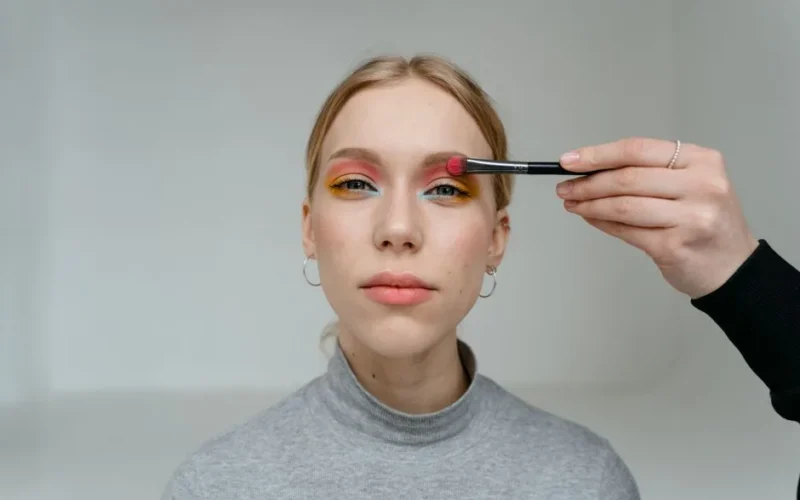 Close-up portrait of a woman having vibrant eyeshadow applied with makeup brush.