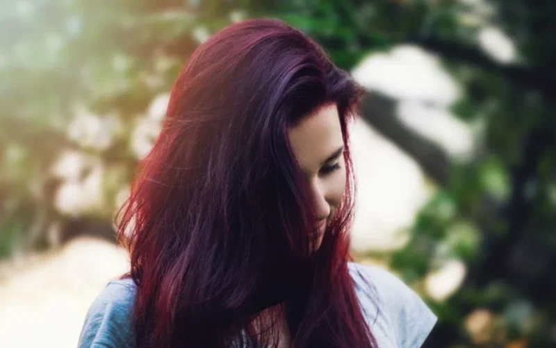 A thoughtful portrait of a young woman with vibrant red hair outdoors.