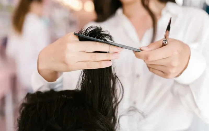 Professional hairdresser cutting hair with scissors and comb in a salon setting.