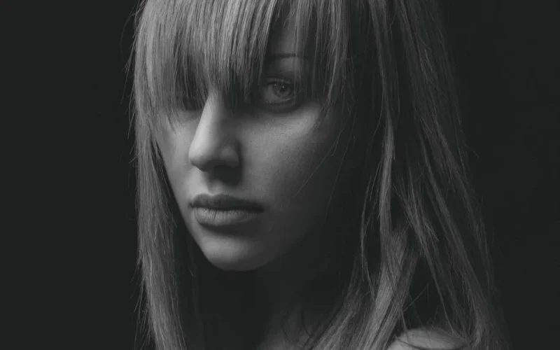 Black and white portrait of a woman with bangs gazing intently, highlighting emotions.