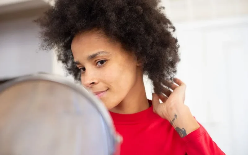 Confident woman with afro hairstyle glancing in the mirror, adjusting her hair indoors.