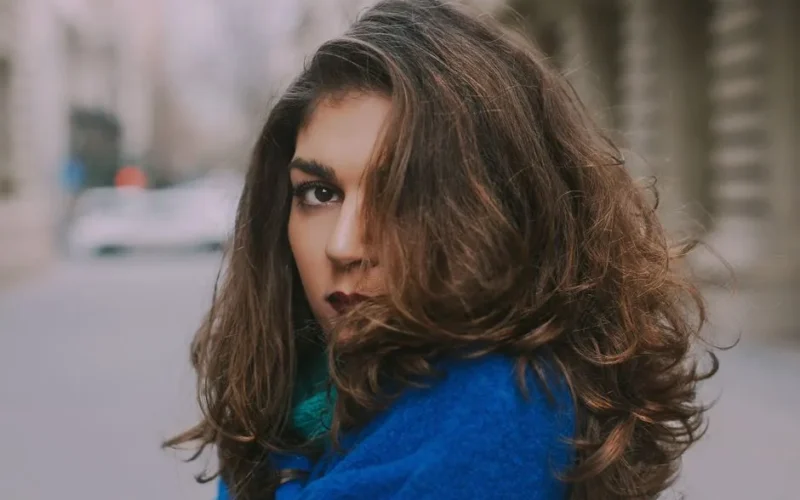 Captivating outdoor portrait of a woman in a blue coat with voluminous hair.