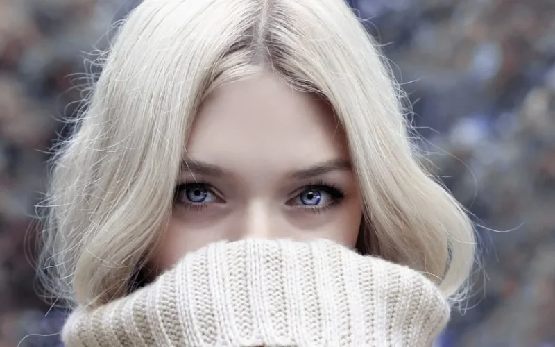 A close-up portrait of a blonde woman in winter attire, emphasizing her eyes.