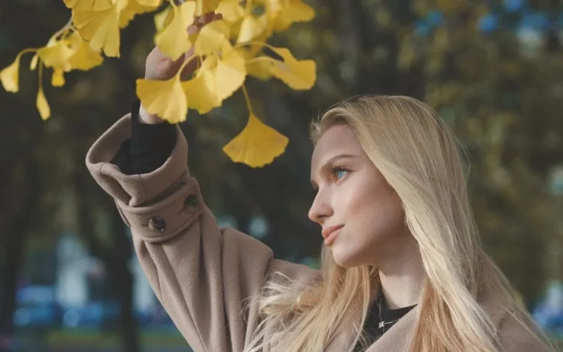 Blonde woman in fall fashion with gingko leaves in a park setting.