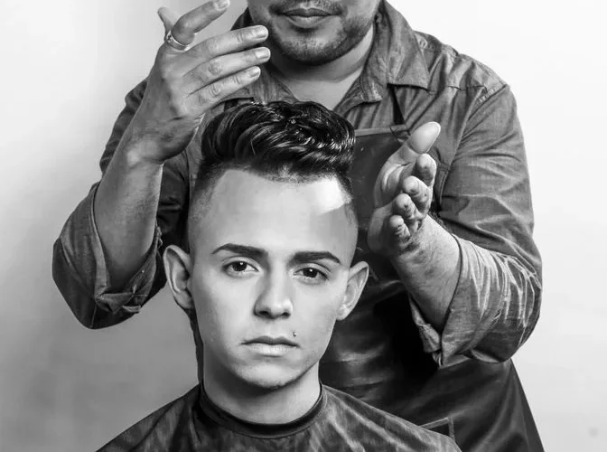 A hairstylist carefully styles a young man's hair in a professional salon setting, emphasizing modern grooming techniques.