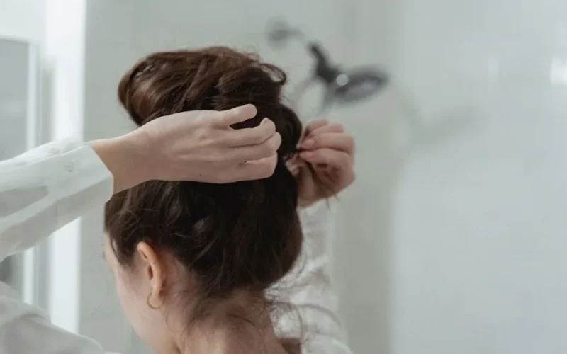A woman styles her hair into an elegant bun in a bathroom setting, focusing on hair care.