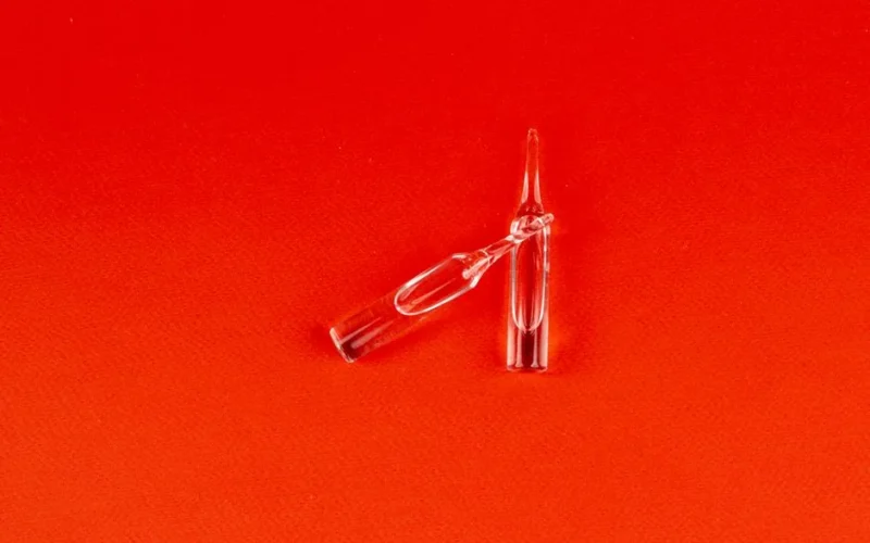 Two clear glass ampoules displayed on a vibrant red surface, showcasing a top view perspective.