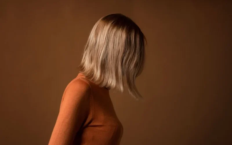Side view of woman with blonde hair in studio with brown background.