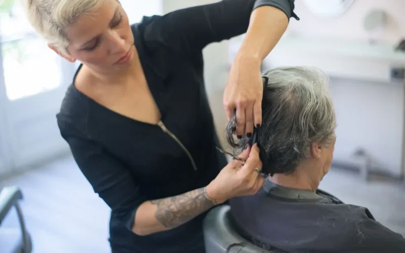 A hair stylist with a tattoo cutting a client's hair in a salon.
