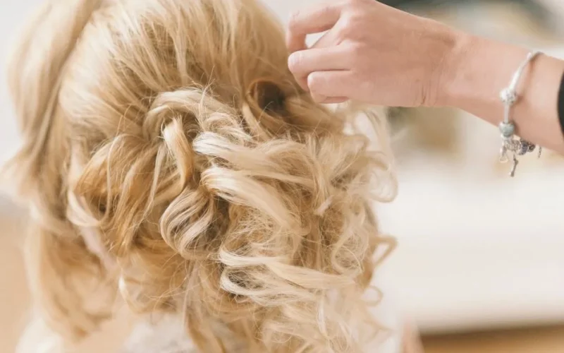 A professional hairstylist creates a blonde bridal updo for a wedding.