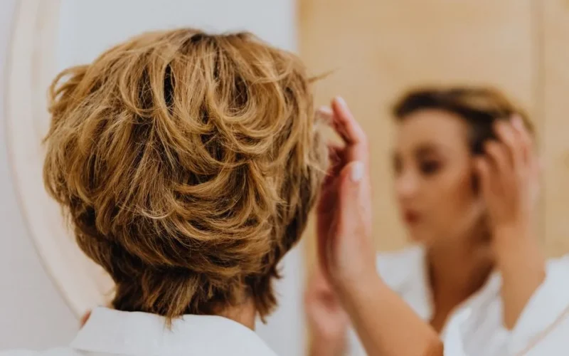 Back view of a woman styling her short hair while looking in the mirror.